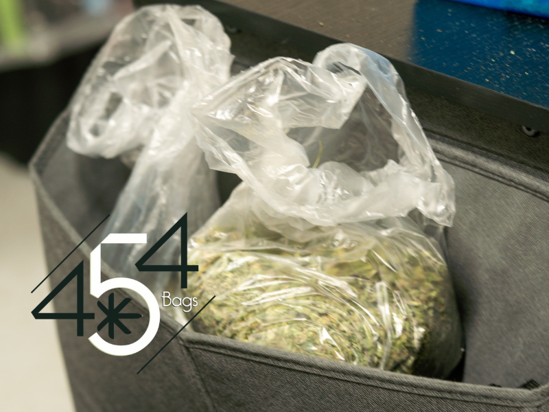 A close-up photo of a black fabric container filled with cannabis buds stored in clear plastic bags, with the logo "454 Bags" prominently displayed in the foreground.