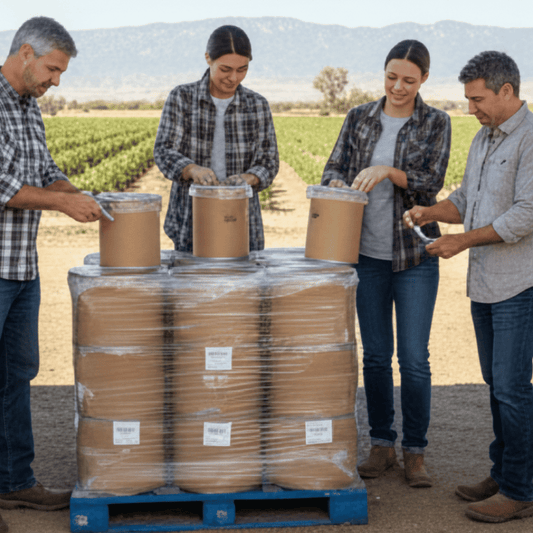 Four people standing around a pallet of stacked brown barrels in an outdoor setting.